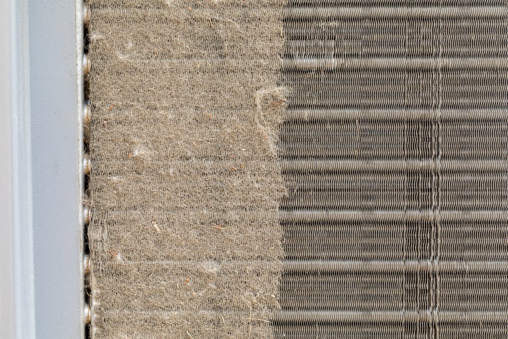 Close-up of a severely impacted commercial RTU condenser coil blocked by dust and cottonwood, causing high head pressure and increased compressor amp draw.
