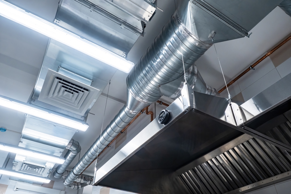 High-bay industrial ventilation system with drop-down supply ducts designed to break thermal stratification and remove machinery heat load in a manufacturing plant.
