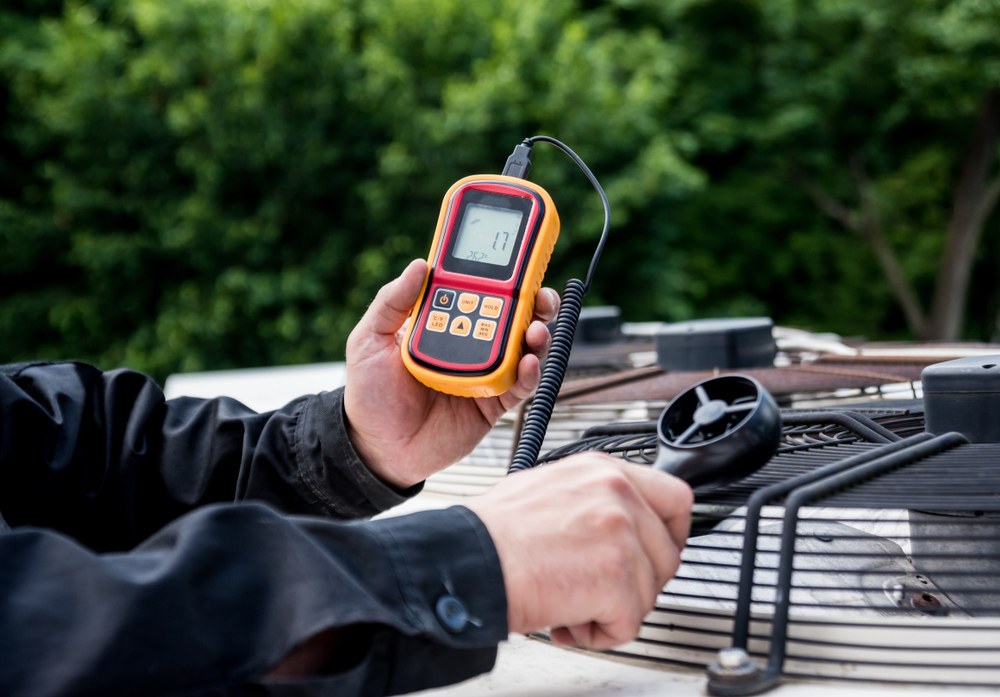 Technician using a digital manometer to measure static pressure (inches of water column) and verify airflow CFM in an industrial ventilation system.
